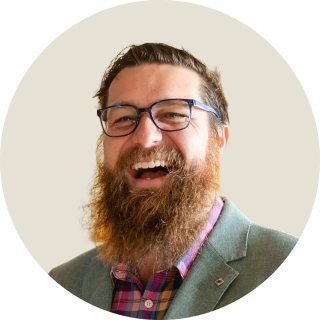 Smiling bearded man in glasses and a colourful shirt wearing a blazer.